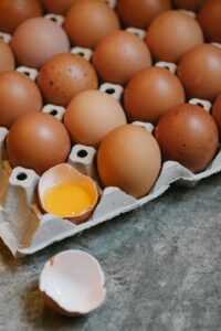 High angle of raw brown chicken eggs placed in recycled carton container on marble table